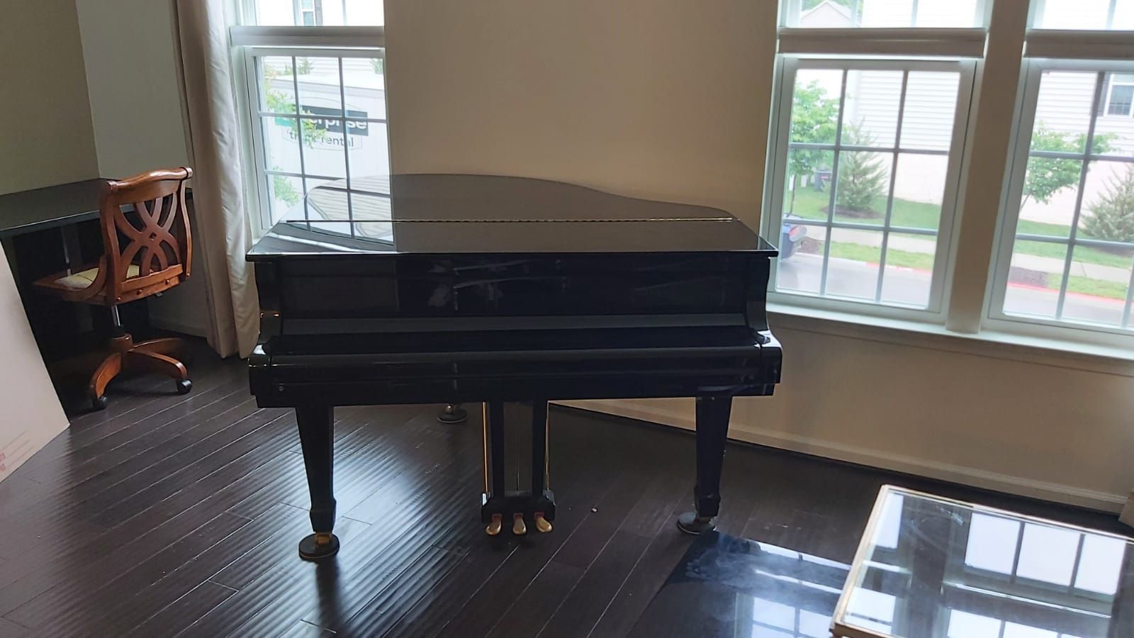 Black piano in a room with hardwood floors, next to a window and desk.