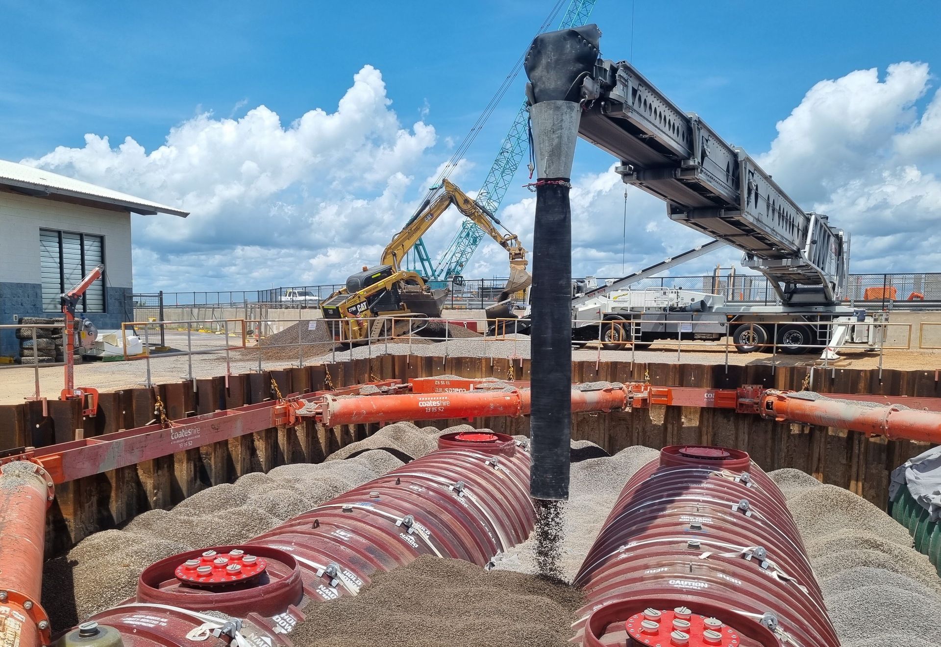 A man in a hard hat is standing next to a conveyor belt filled with concrete.