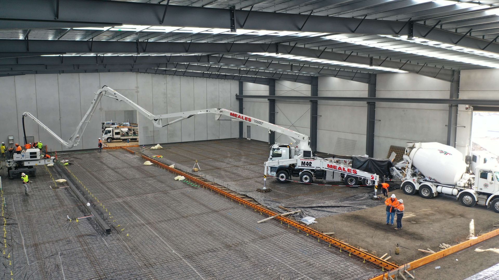 A concrete pump is being used to pour concrete into a large warehouse.