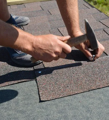 Roofer installing Asphalt Shingles on a house construction roof corner with a hammer and nails. Roofing construction with Asphalt Shingles
