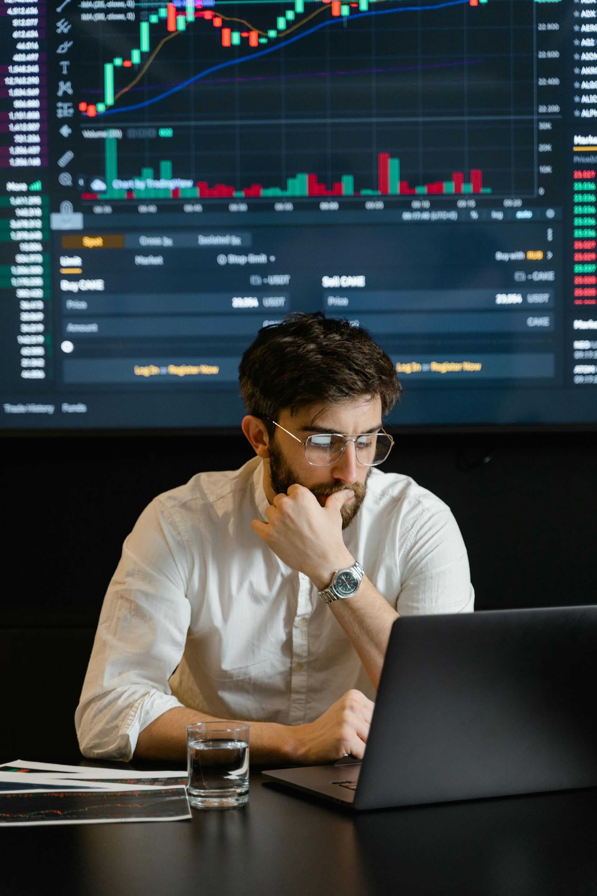 A man is sitting at a table looking at a laptop computer.