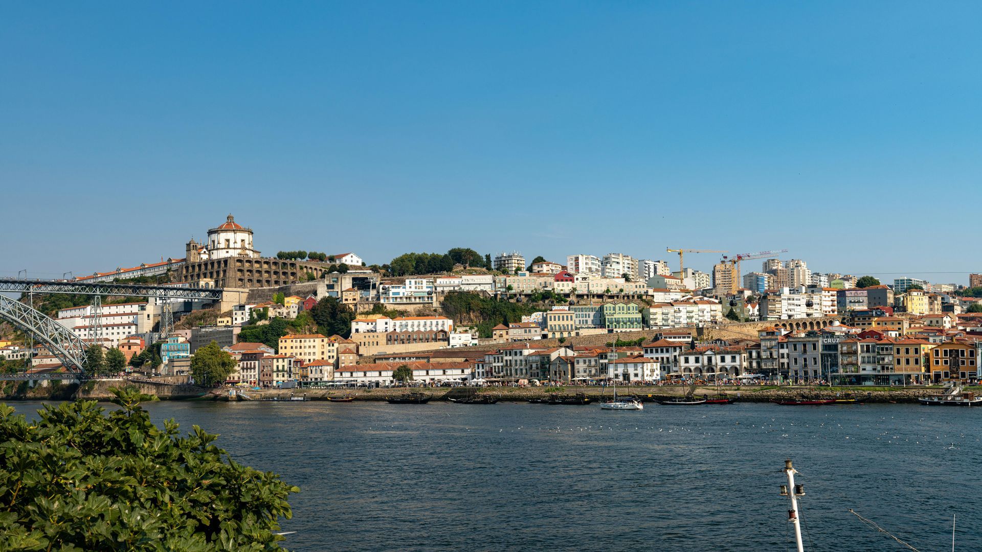 Cityscape of Porto, Portugal, with colorful buildings on a hillside overlooking a river under a clear blue sky.