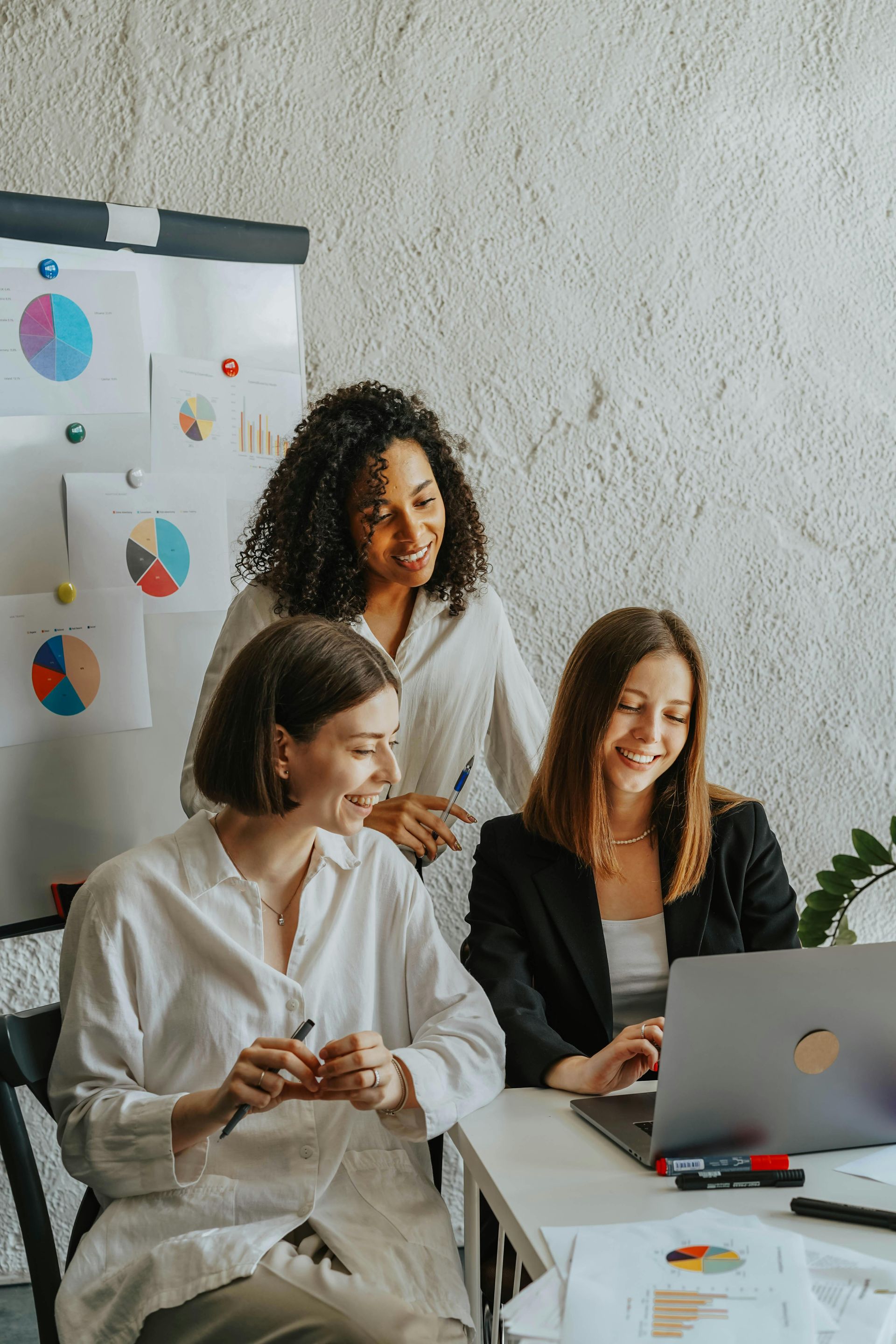 Three women are sitting at a table looking at a laptop computer.