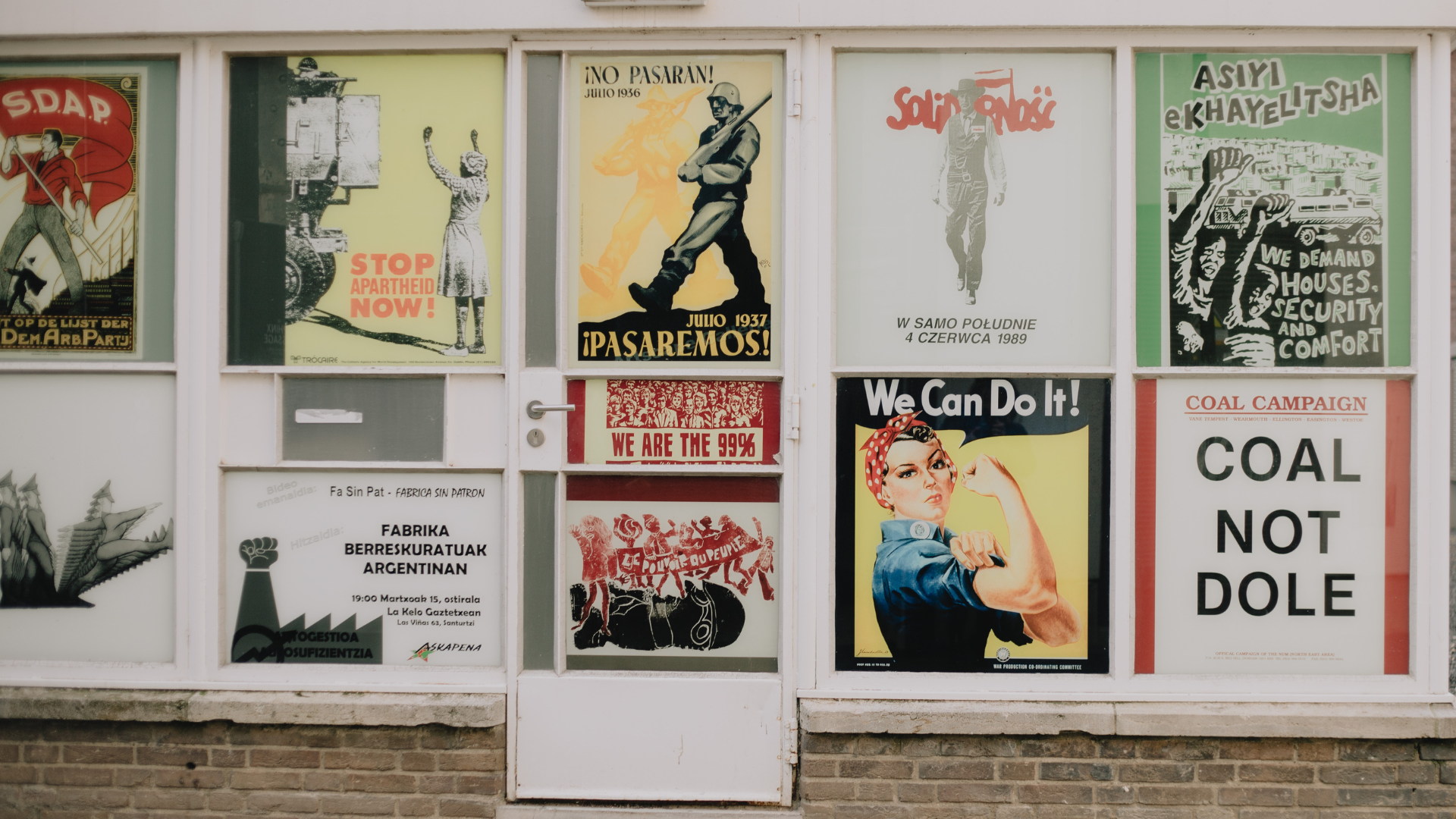 Window display with various vintage posters: protest slogans, Rosie the Riveter, a soldier.