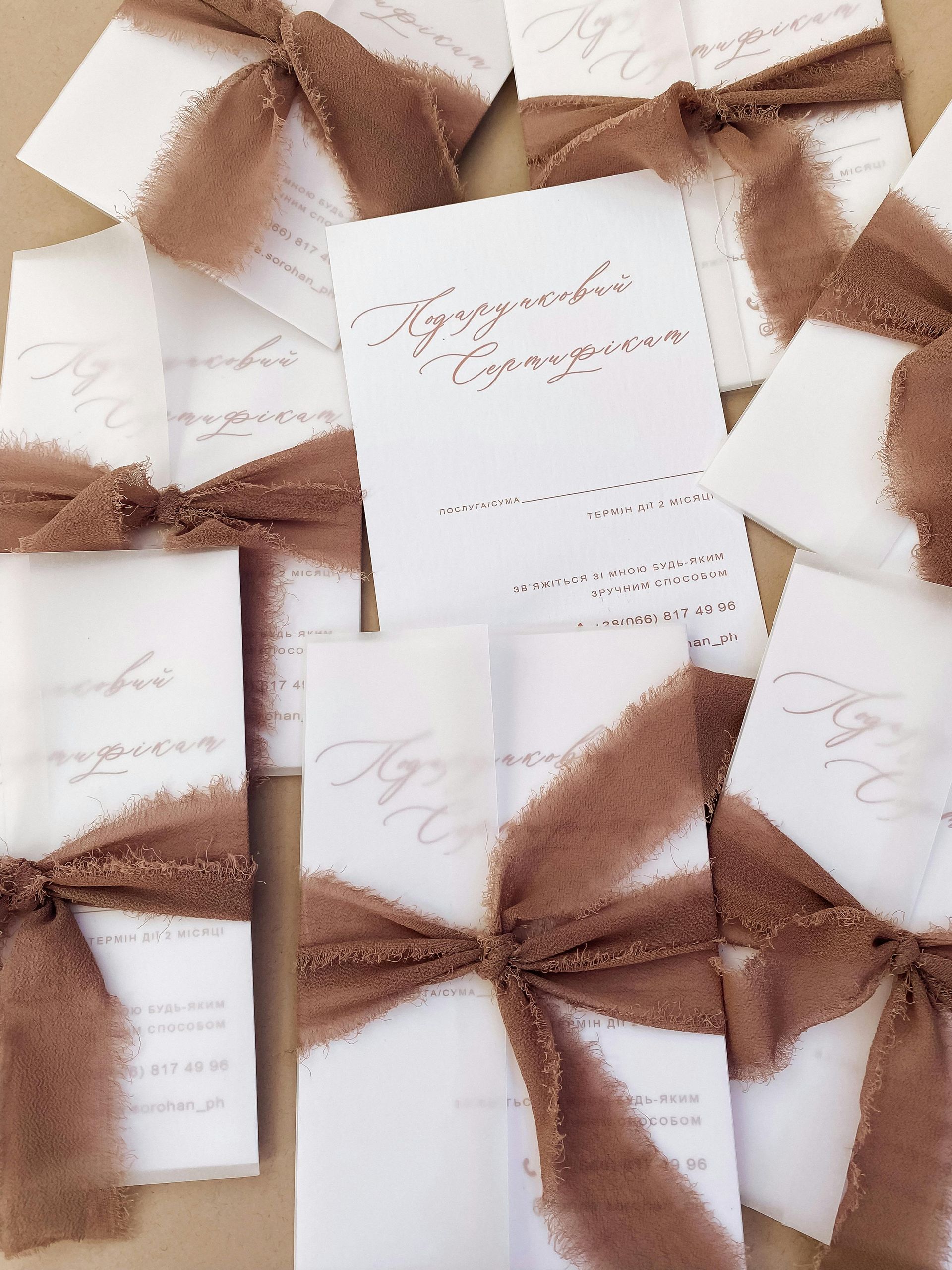 White cards with brown ribbon bows, scattered on a light brown surface.