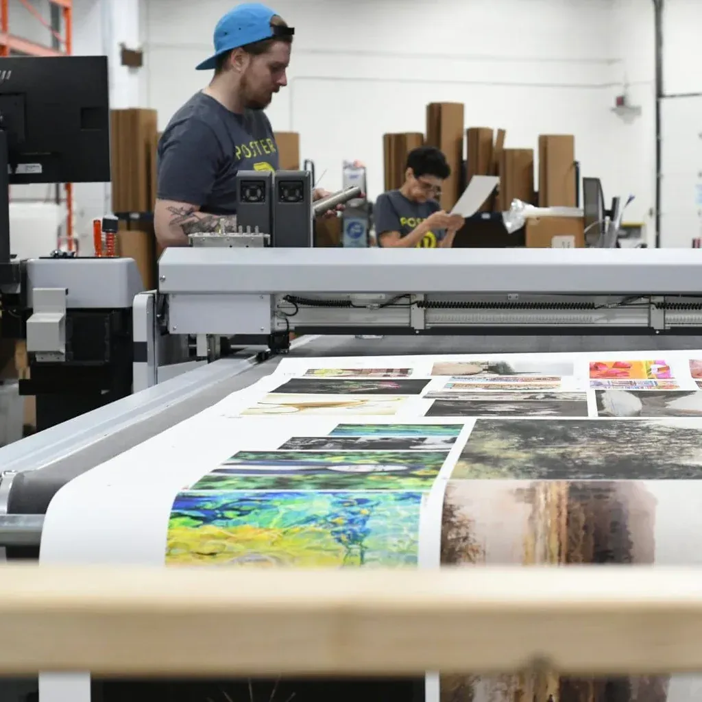 Man and child operating large-format printer, reviewing printed images in a warehouse setting.