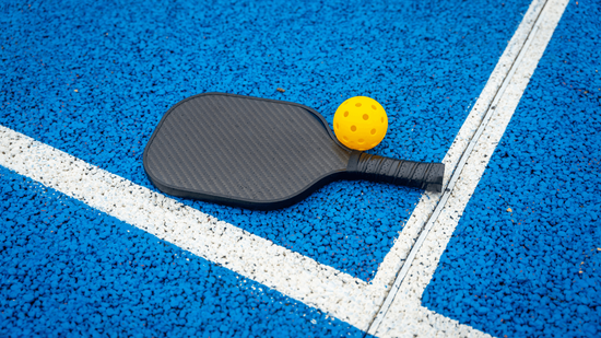 “Pickleball paddle and yellow ball resting on a textured blue court with white lines during a court builder service in Henderson, NV”