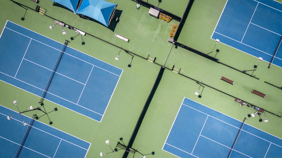 “Aerial view of multiple blue tennis courts inside a large recreational complex during a court builder service in Henderson, NV”