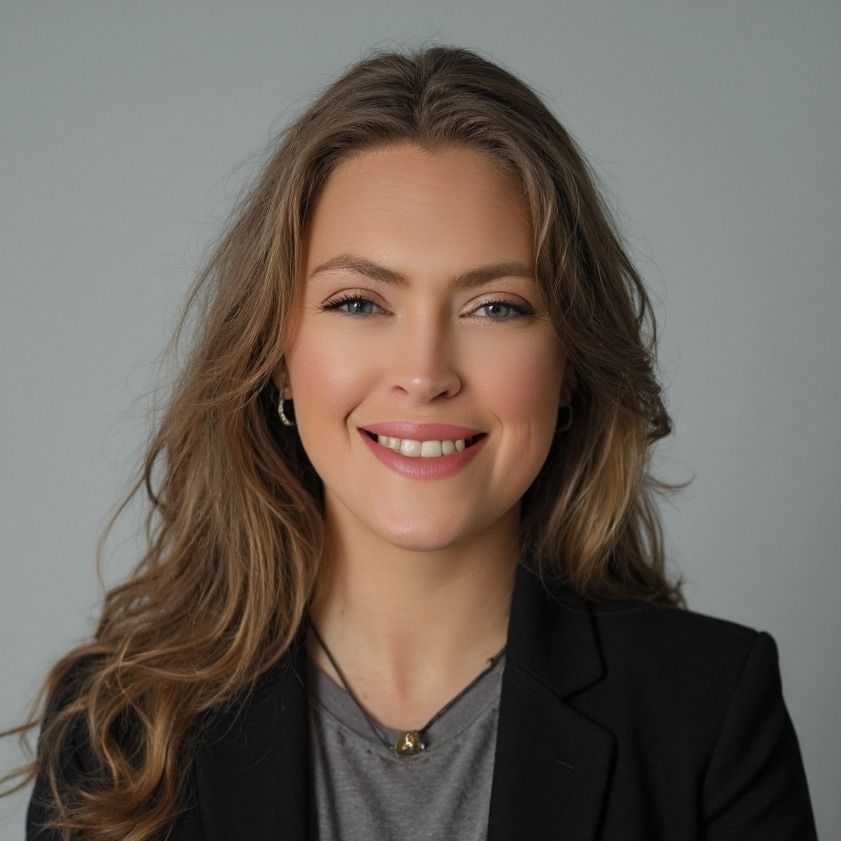 Woman with long brown hair smiling, wearing a black blazer and gray shirt, against a gray backdrop.