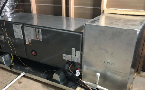 A horizontal HVAC air handler and metallic ductwork installed in an unfinished wooden attic frame.