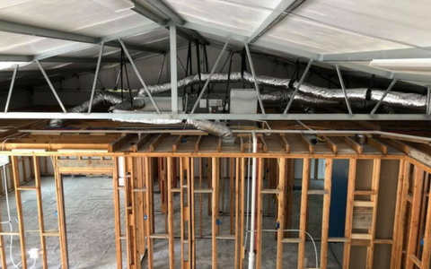 Interior construction showing unfinished wooden wall framing and metal trusses beneath a white ceiling with ductwork.