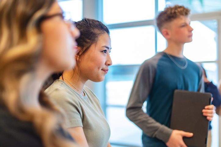 A group of young people are standing next to each other in front of a window.