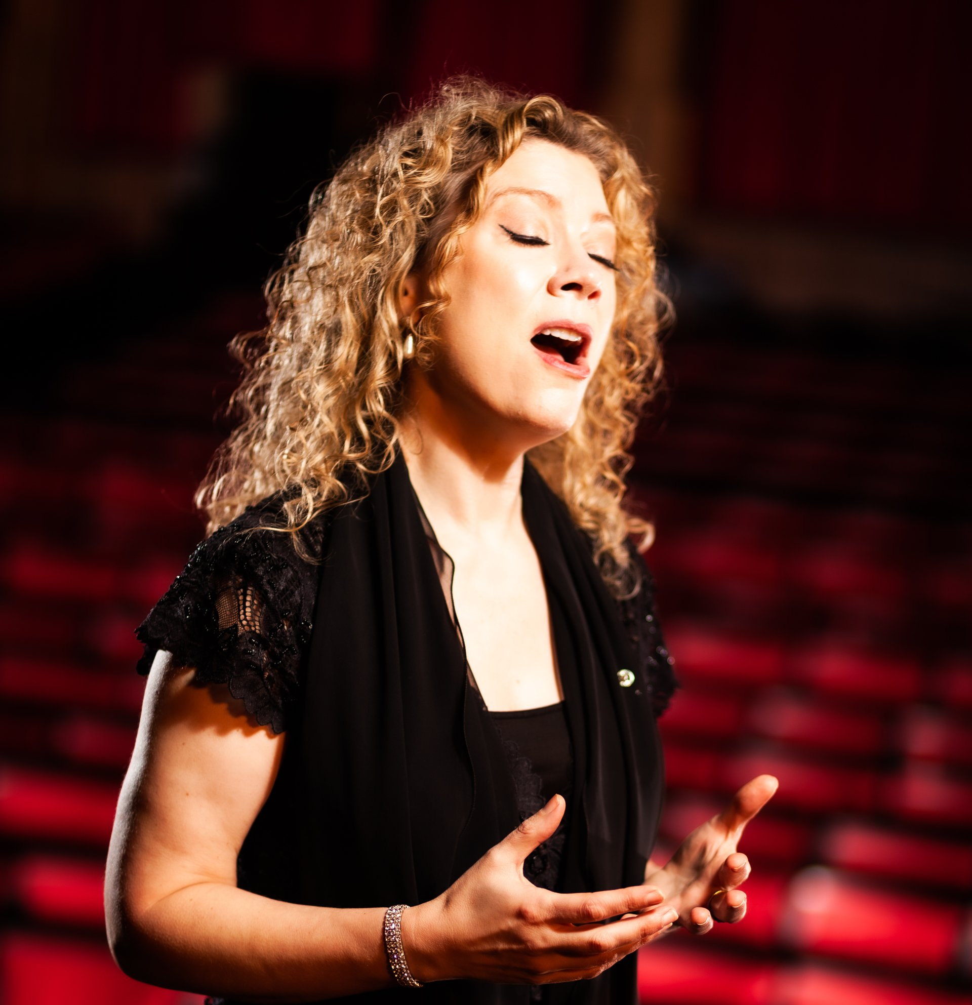 A woman with curly hair is singing in front of red seats