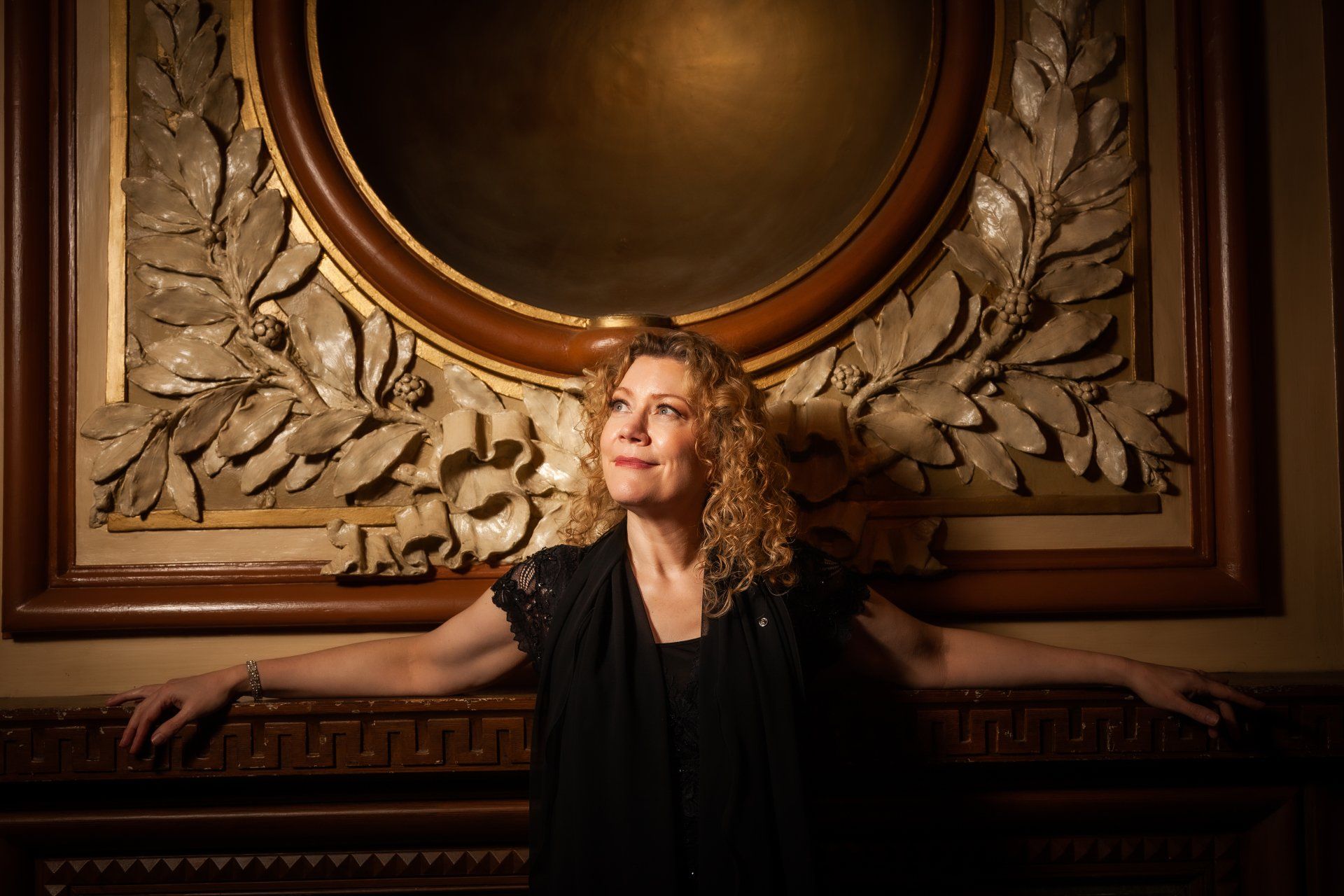 A woman in a black dress is standing in front of a painting.