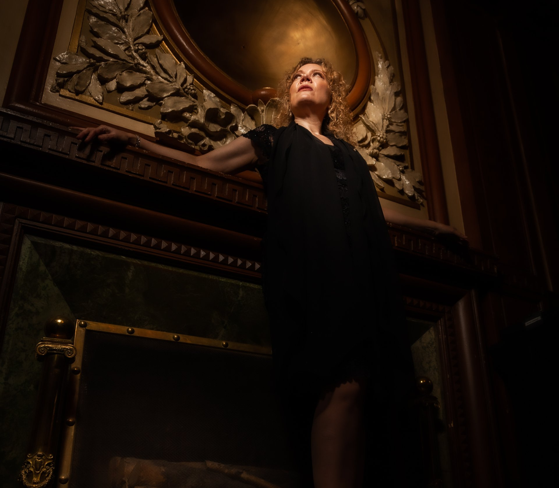 A woman in a black dress is standing in front of a fireplace