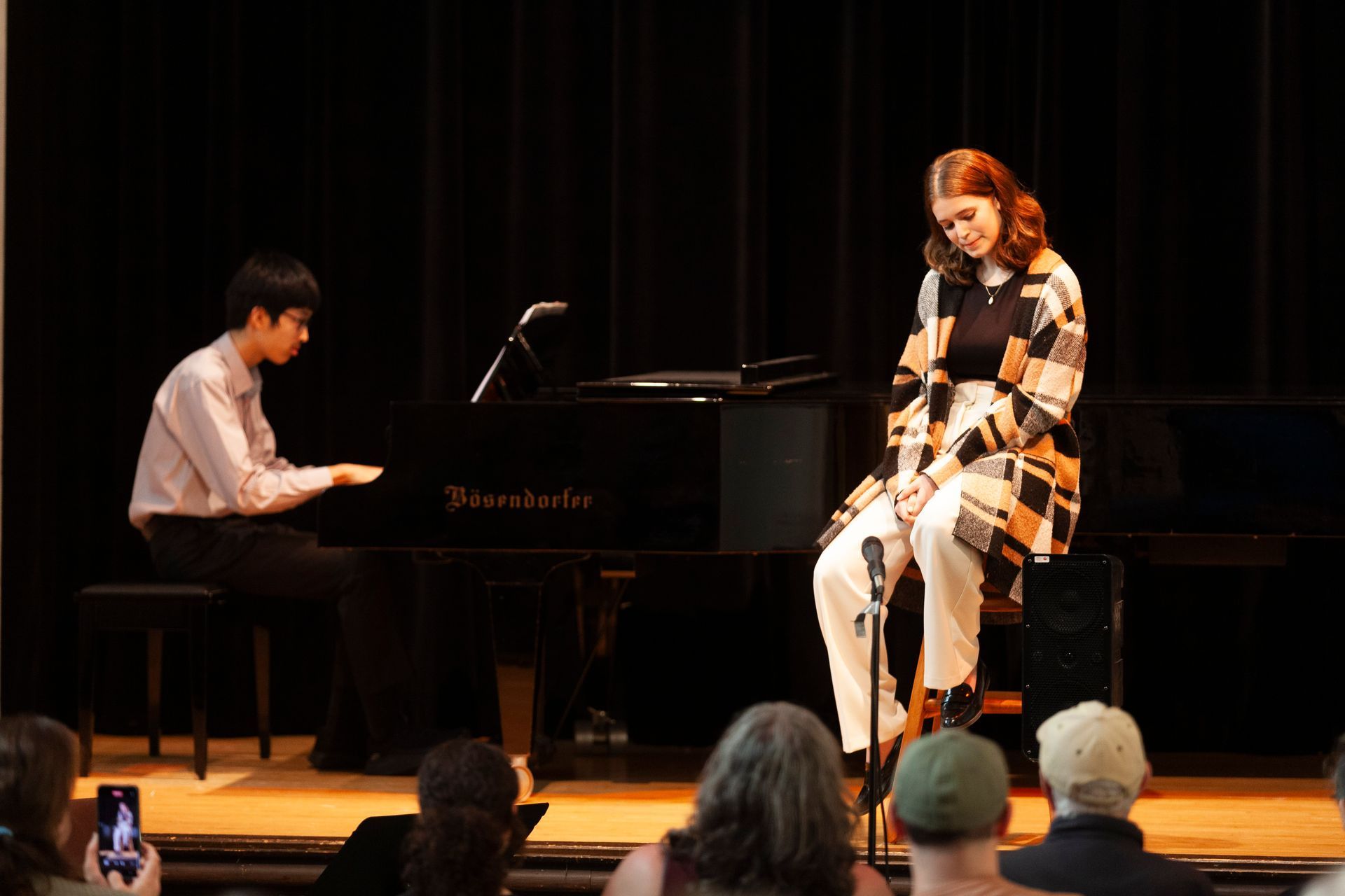A man is playing a piano and a woman is sitting in front of a microphone on a stage.