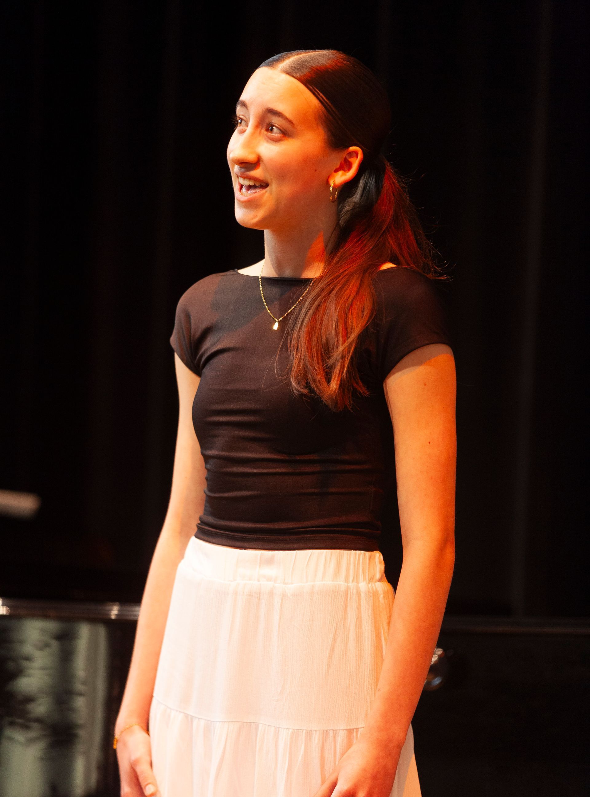 A woman in a black top and white skirt is standing on a stage.