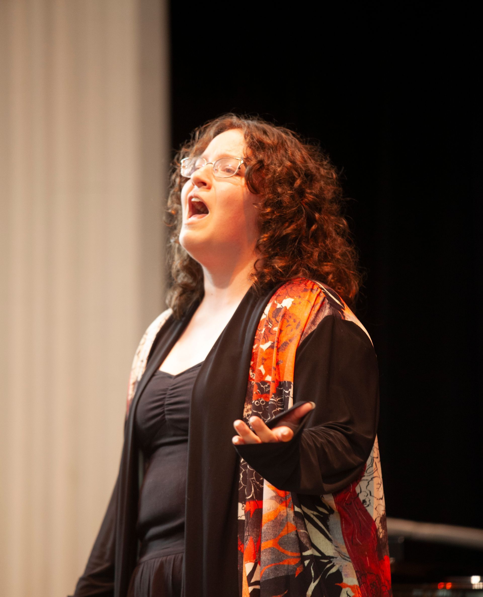 A woman wearing glasses is singing on a stage.