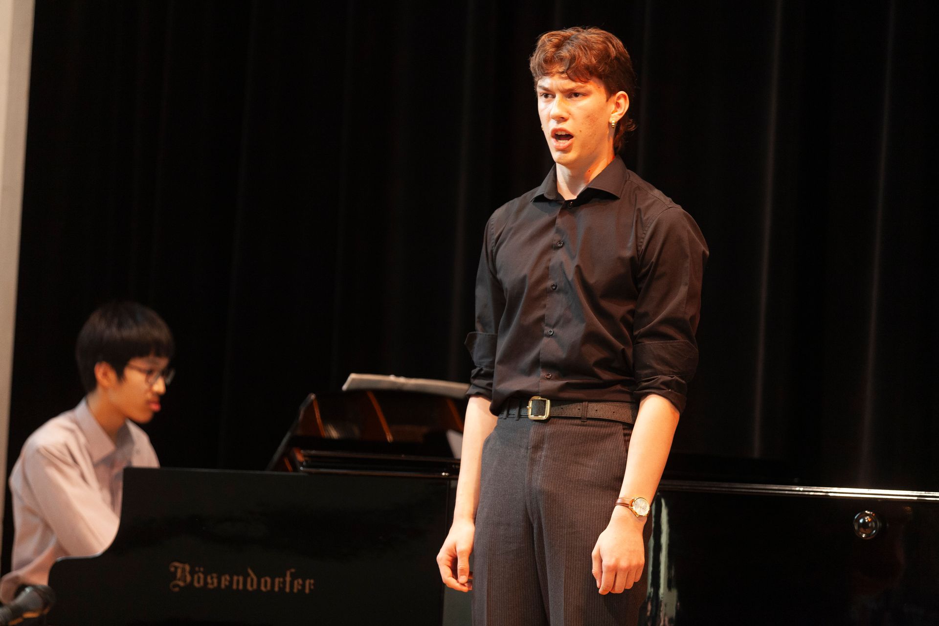 A man is singing on stage while another man plays the piano.