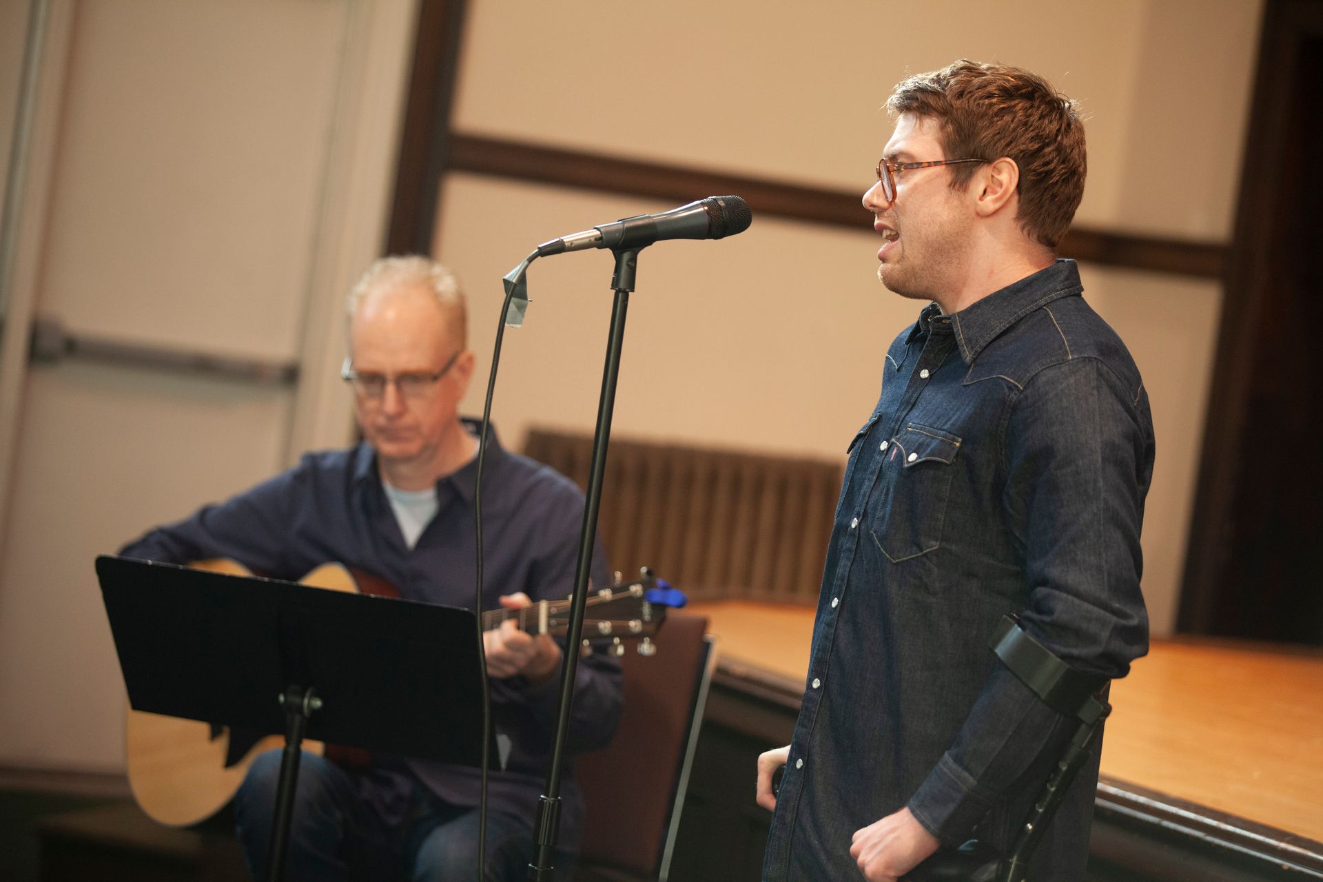 A man singing into a microphone while another man plays a guitar