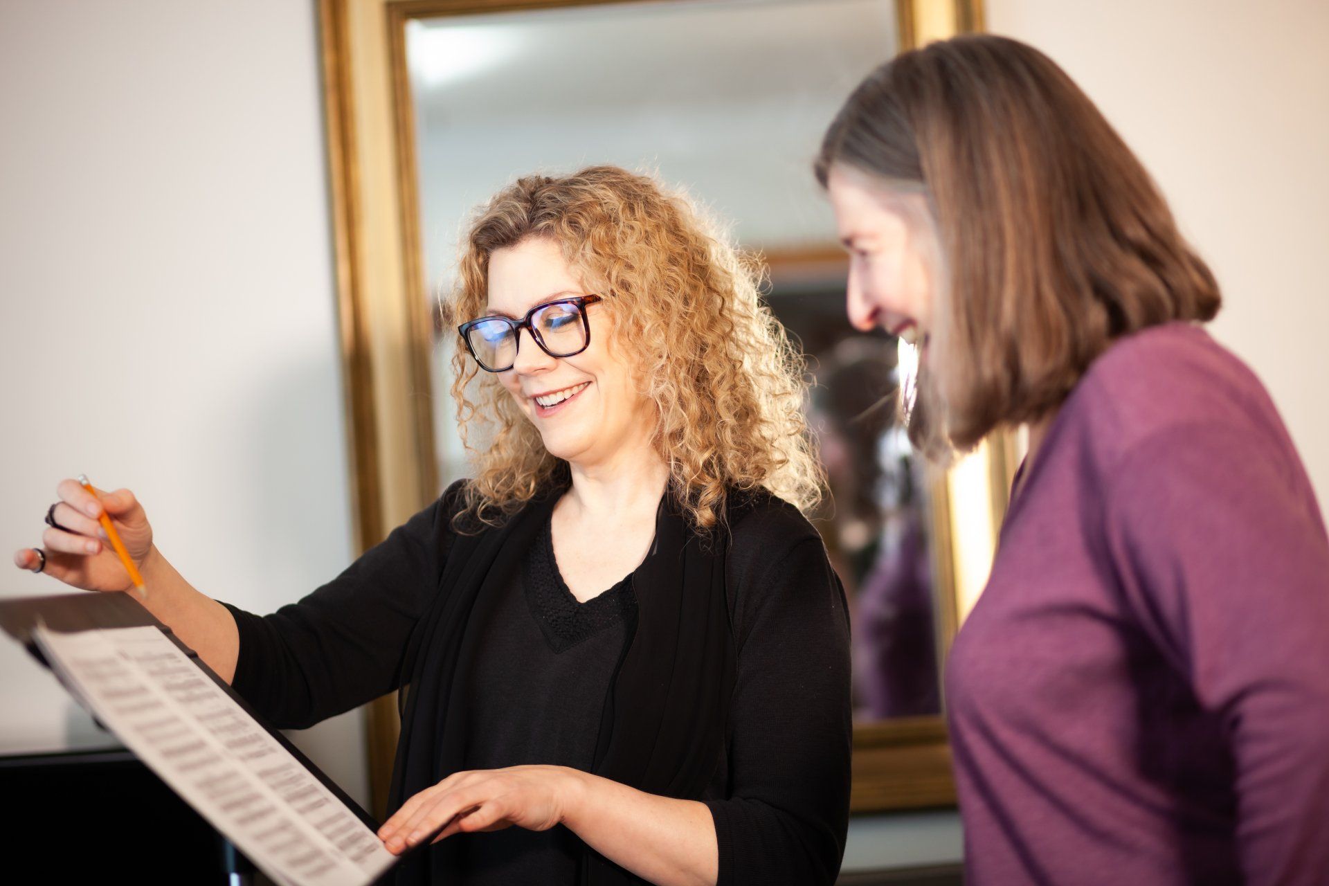 Two women are standing next to each other looking at sheet music.