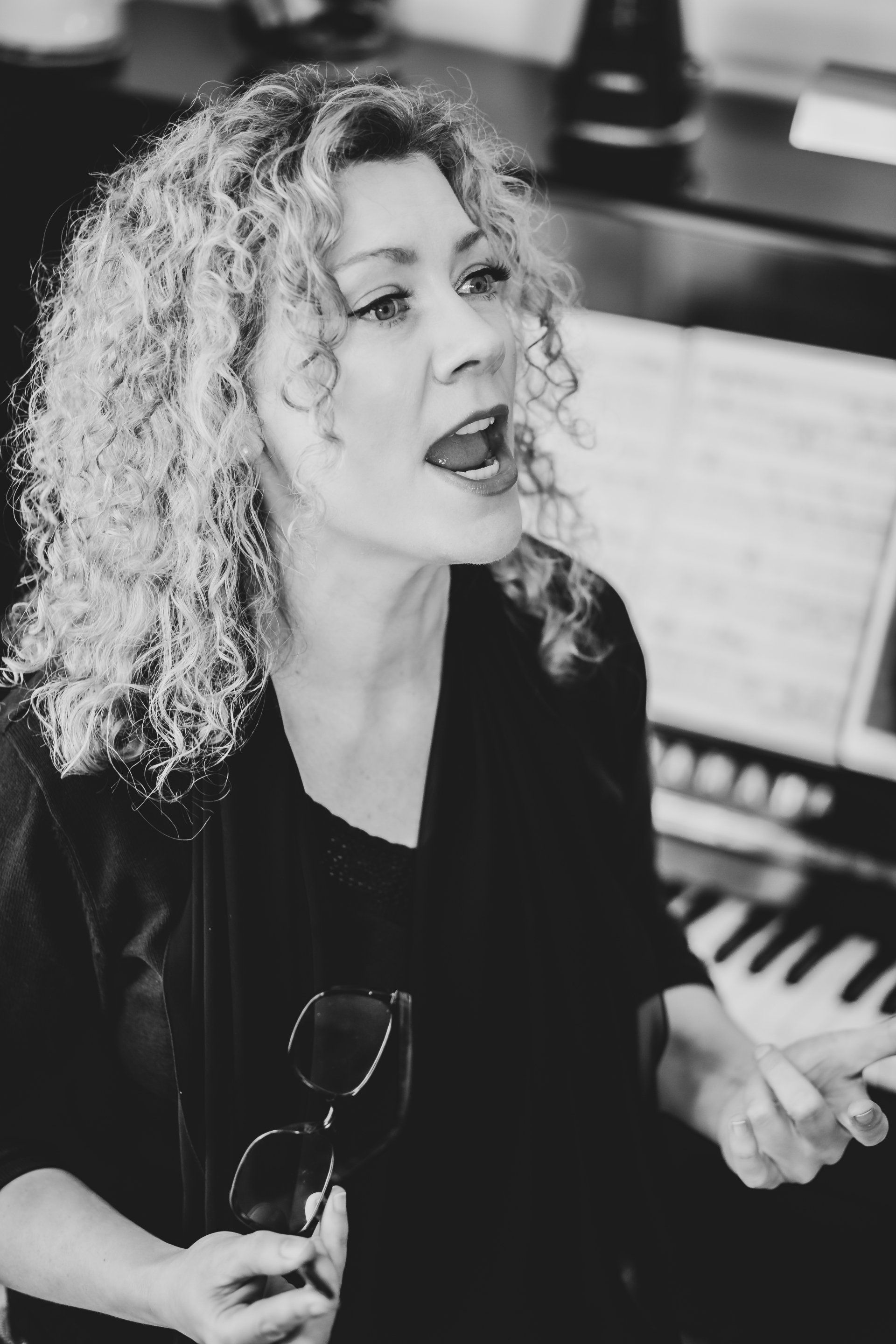 A woman is singing in front of a piano in a black and white photo.
