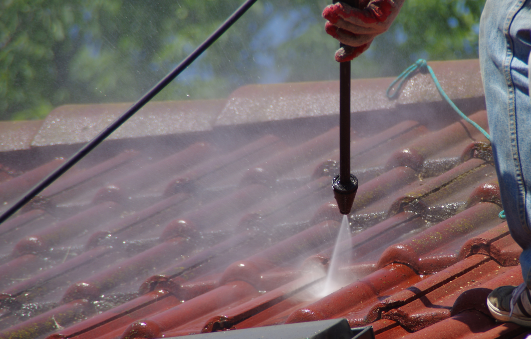 A man is using a high pressure washer to clean a tiled roof.