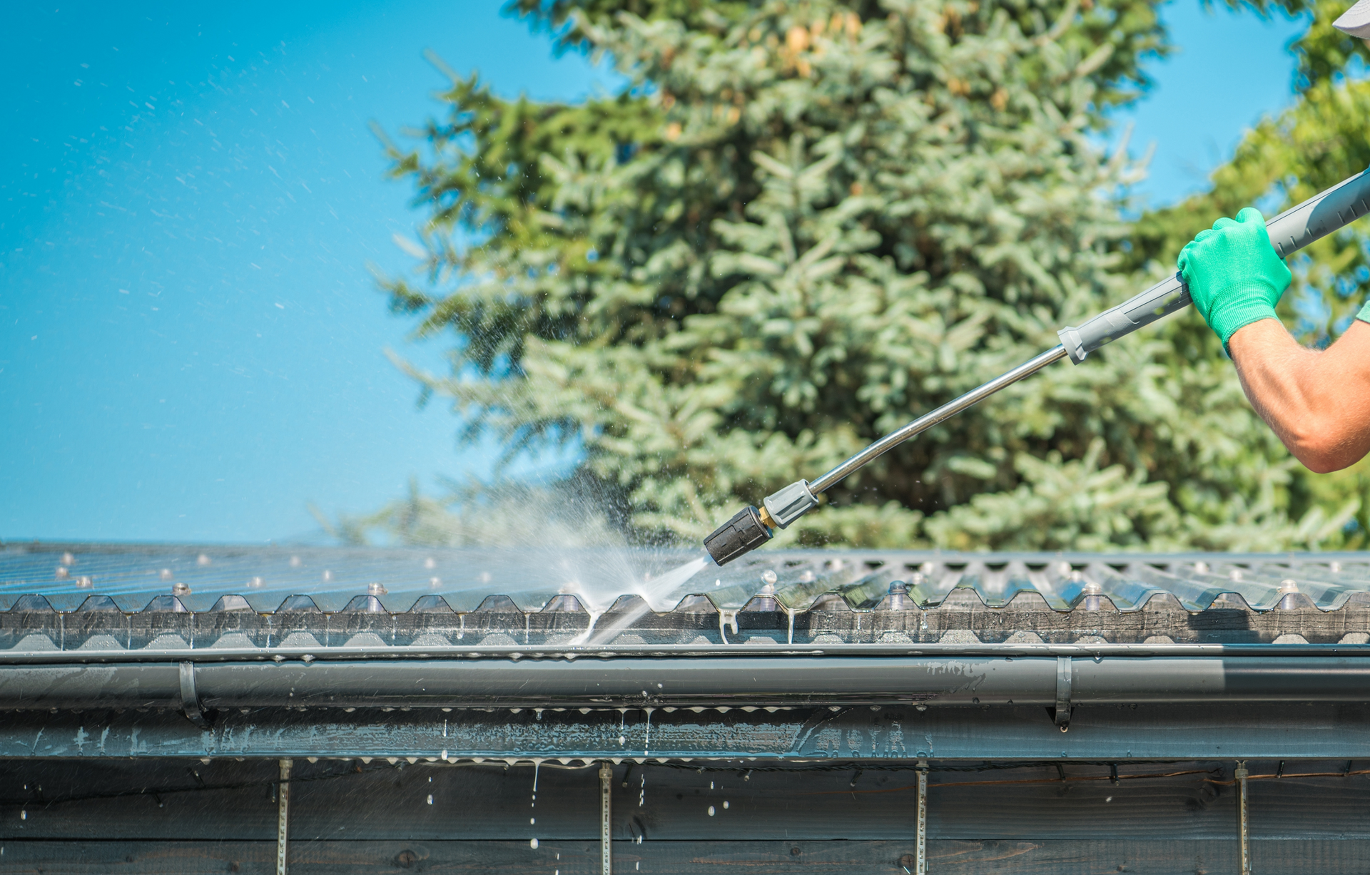 A man is cleaning a gutter with a high pressure washer.