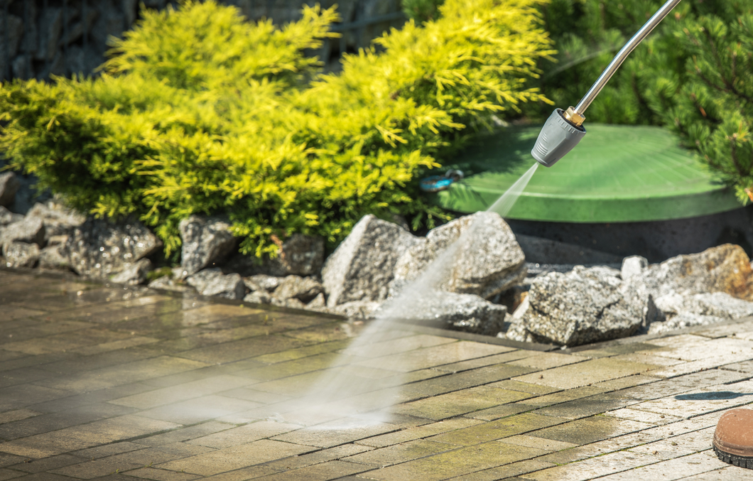 A person is using a high pressure washer to clean a patio.