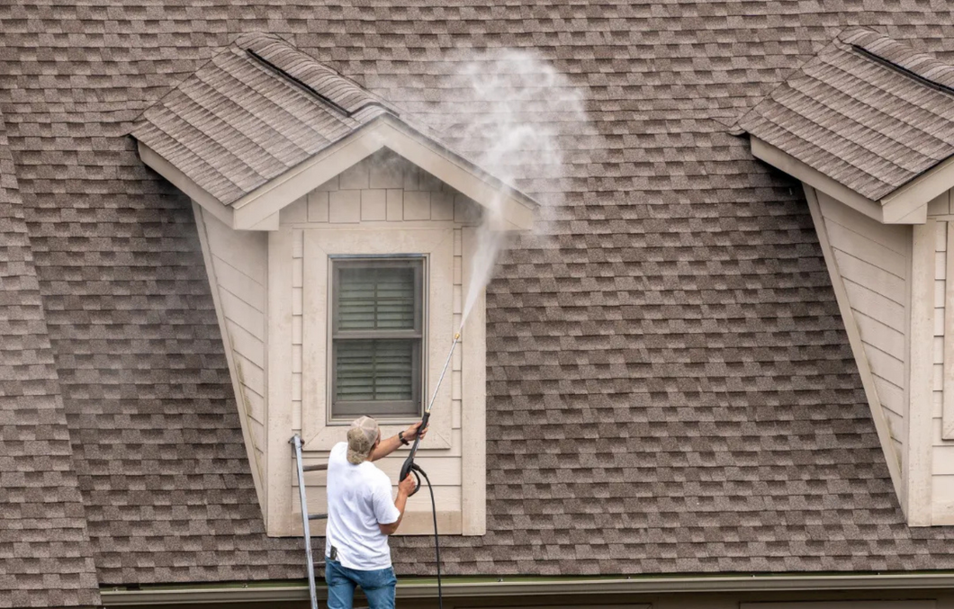 A man is cleaning the roof of a house with a high pressure washer.