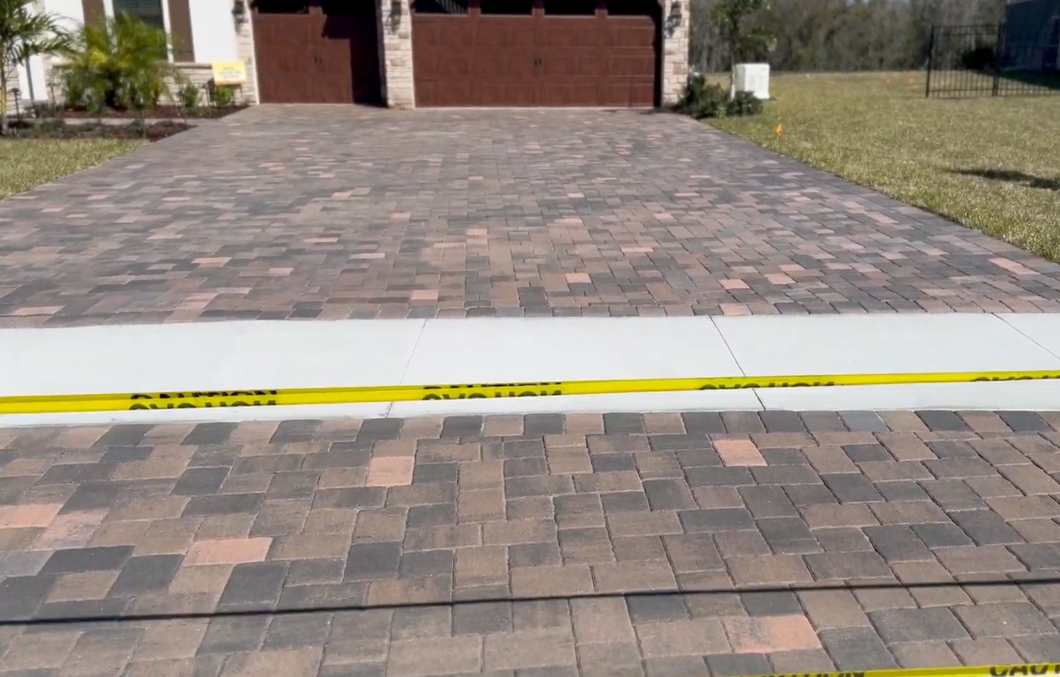A brick driveway with a yellow tape on the side of it.