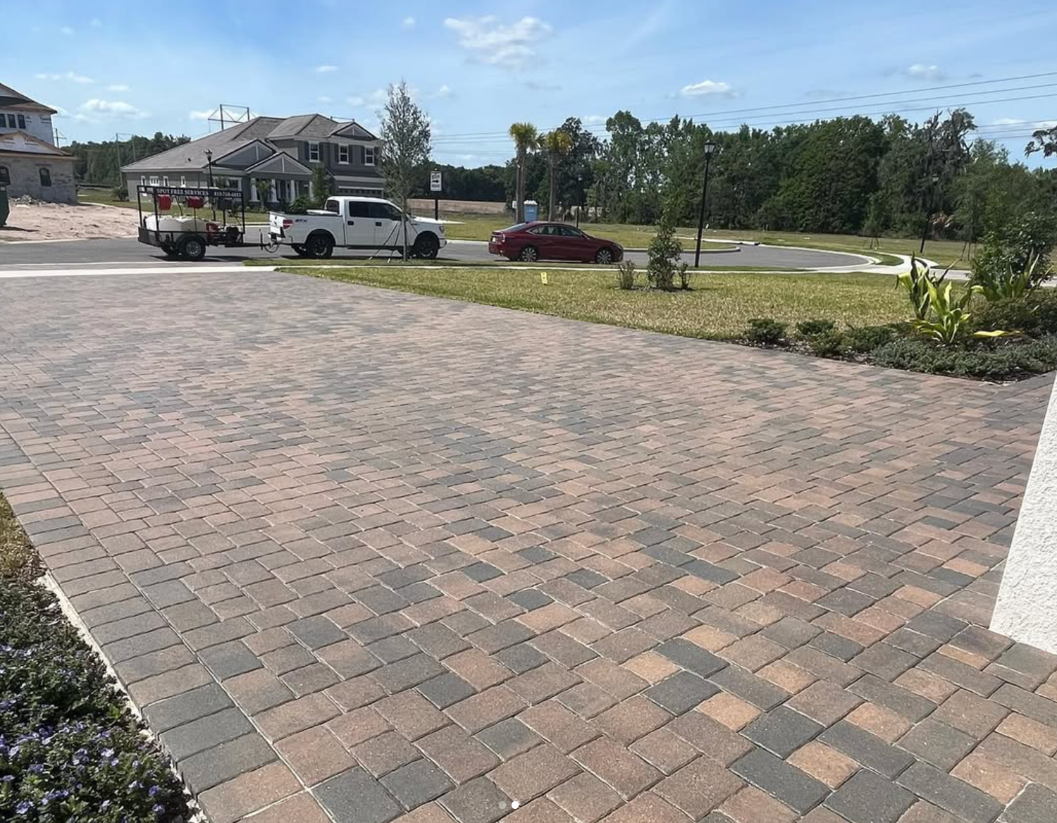 A white truck is towing a red car down a brick driveway.