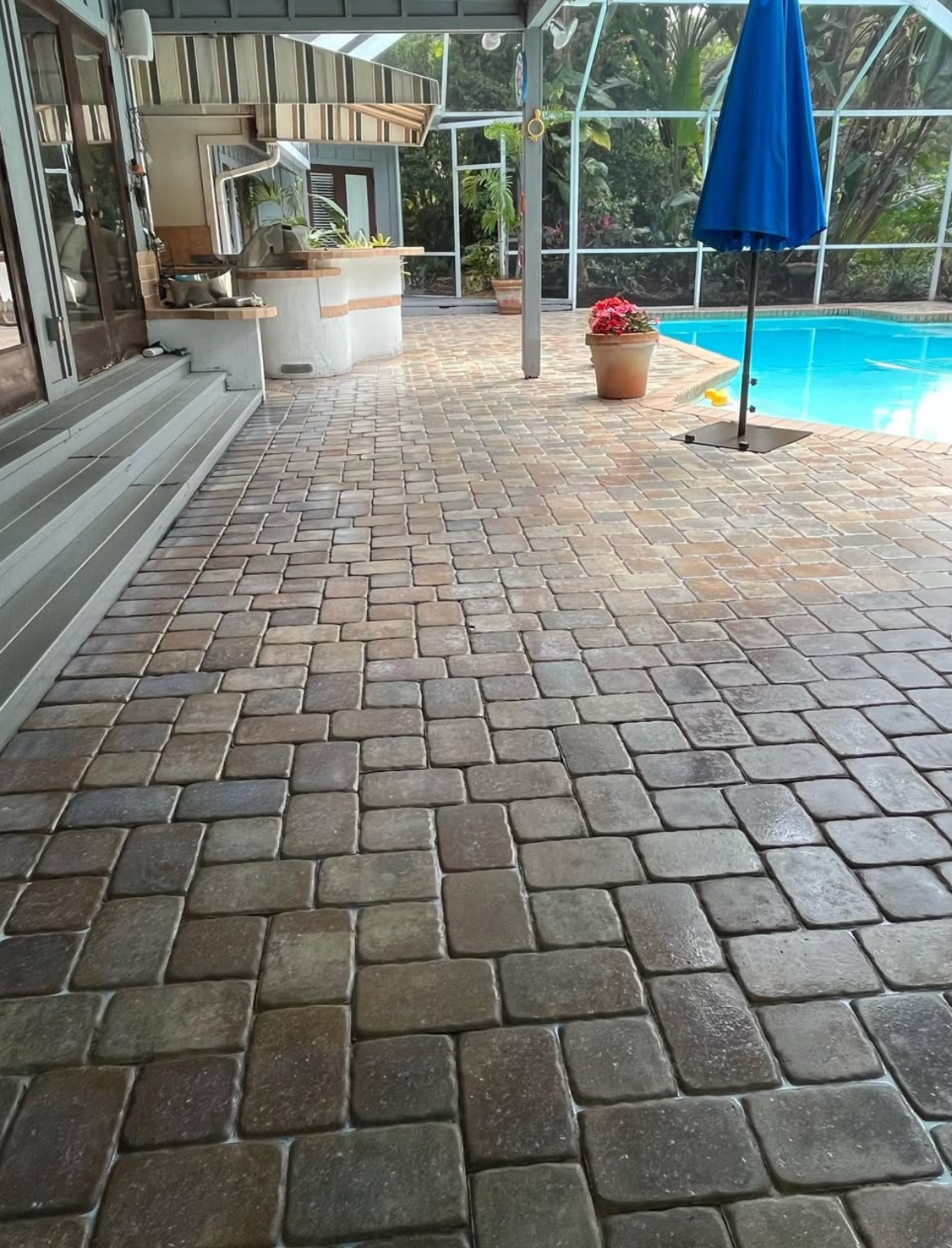 A brick walkway leading to a pool with a blue umbrella