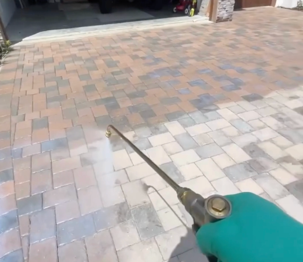 A person is spraying a brick driveway with a sprayer