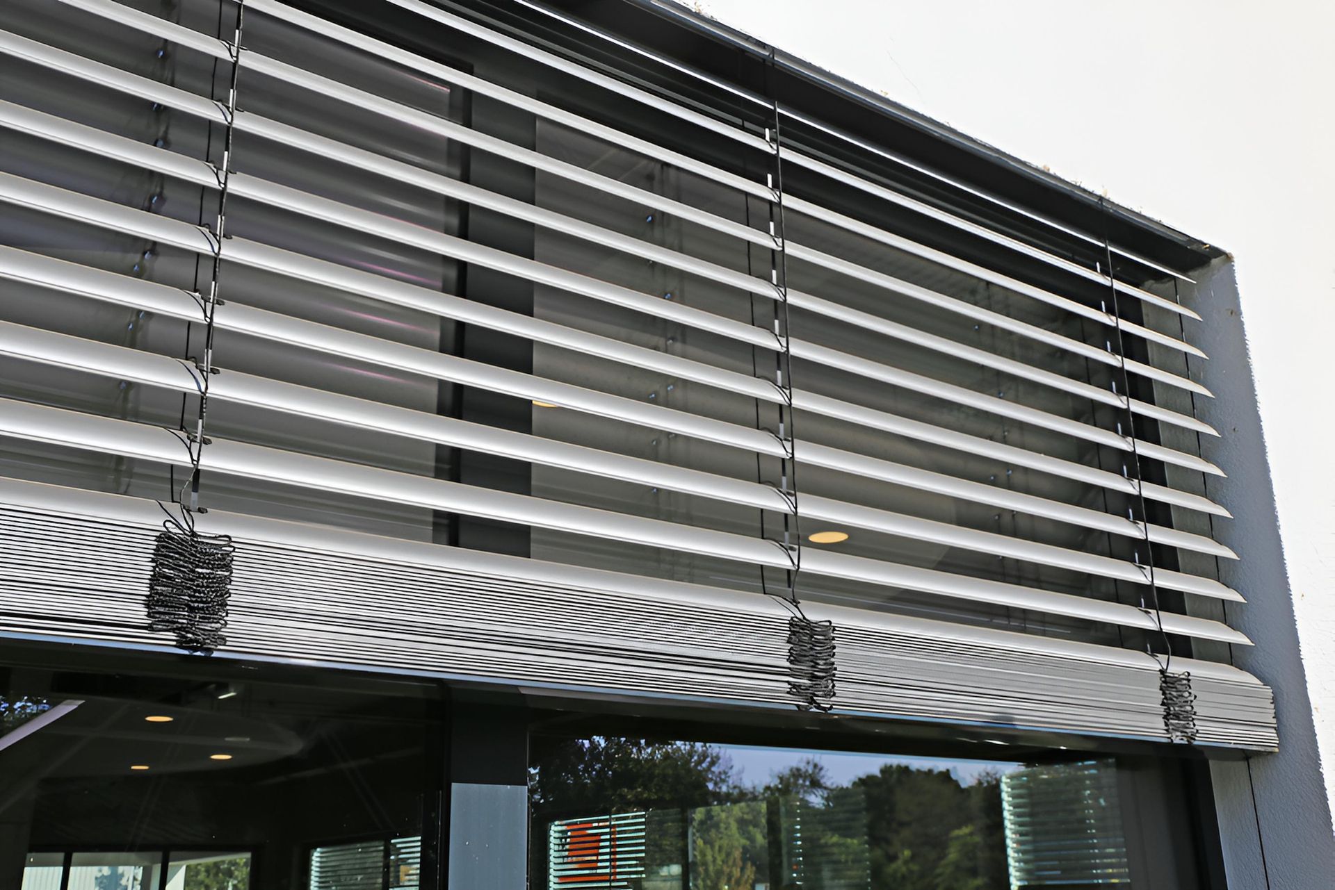 Exterior view of building with horizontal, adjustable sun shades over a large window  — Manning Blinds & Awnings in Taree, NSW