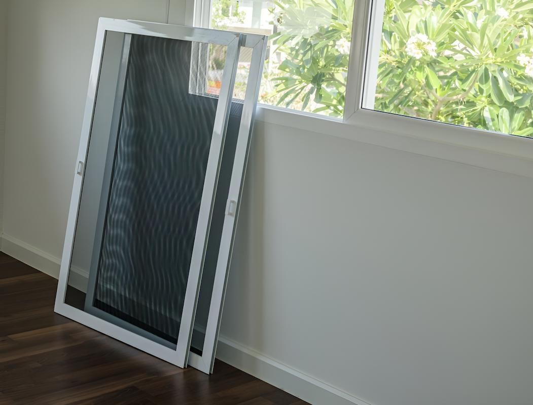 A Screen Door is Sitting on the Floor Next to a Window — Manning Blinds & Awnings in Forster, NSW
