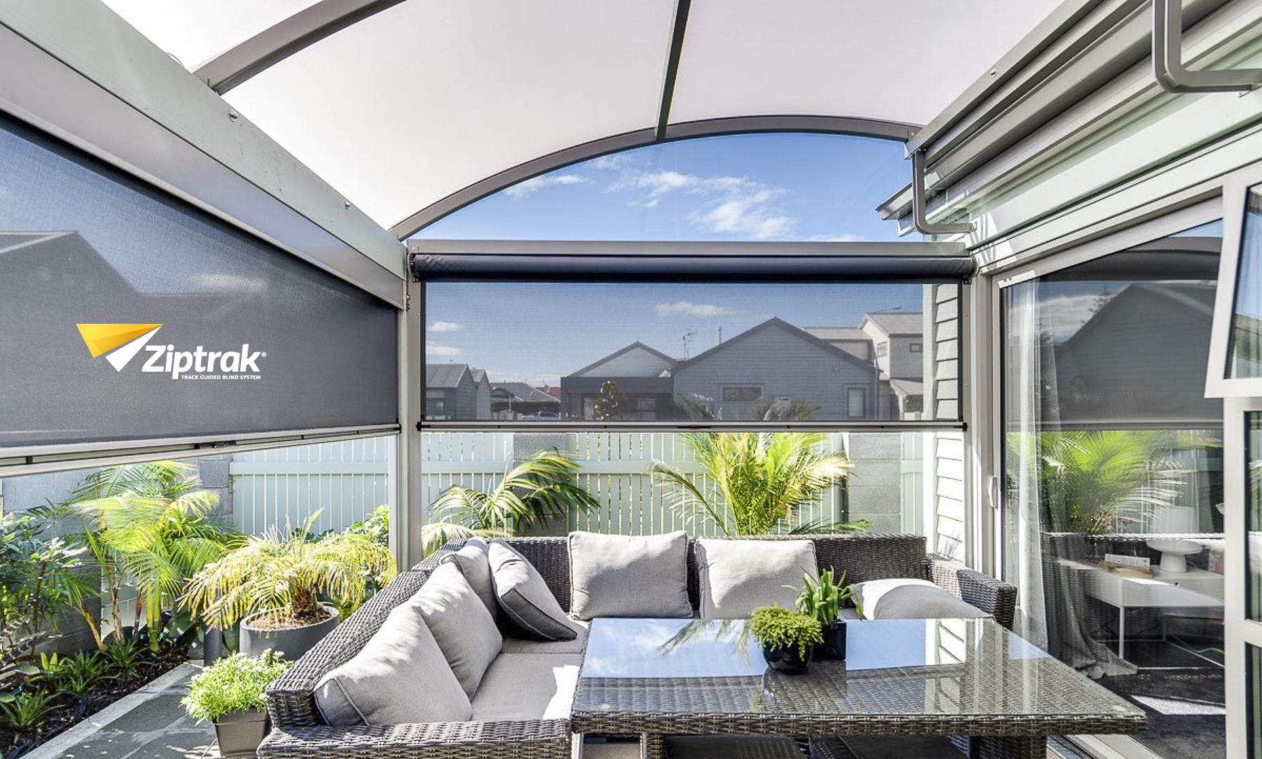 Outdoor patio with gray furniture, ZipTrak shade, and lush greenery — Manning Blinds & Awnings in Taree, NSW