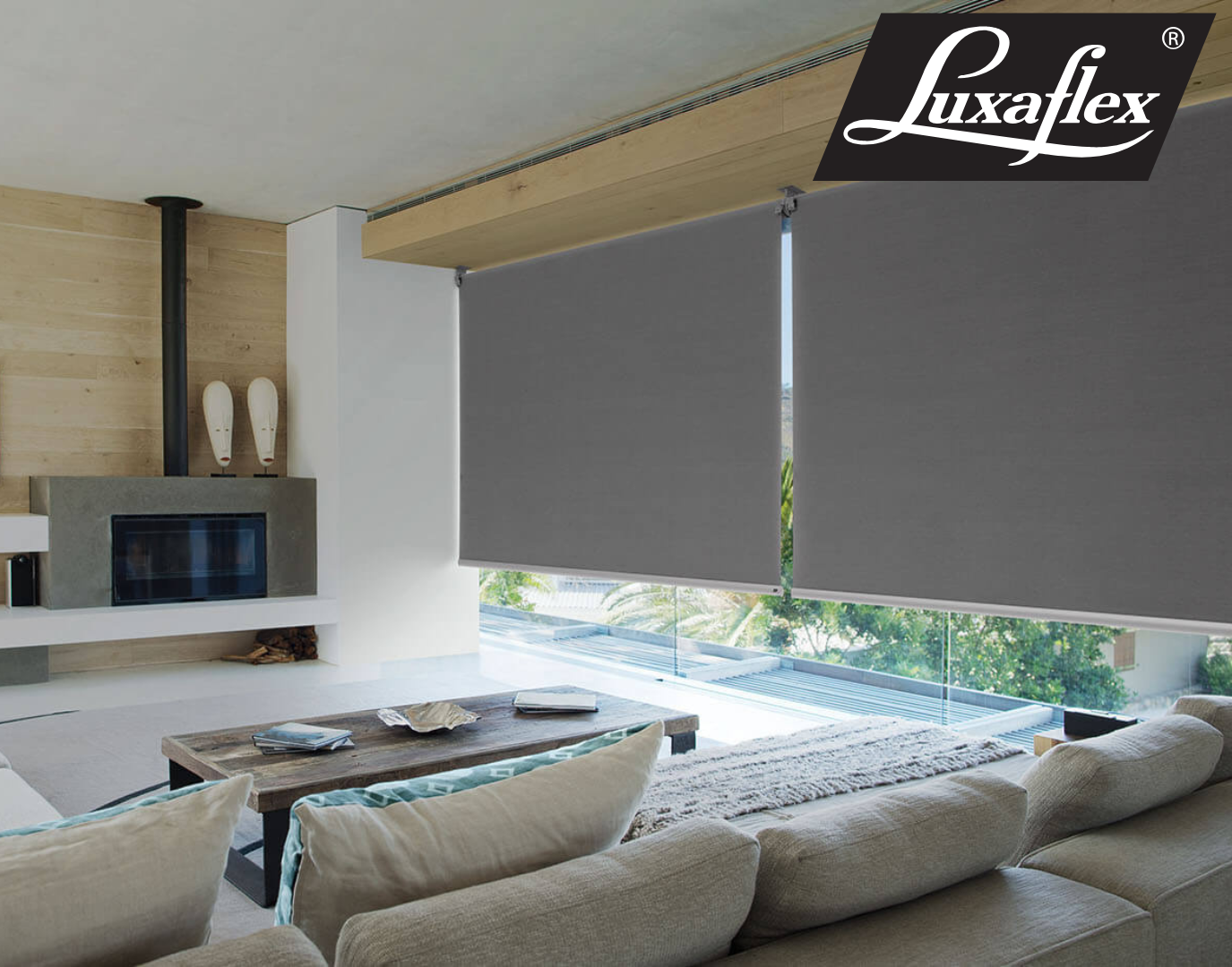 Window seat with a gray cushion and pillow, a closed gray roller shade, and a view of green trees  — Manning Blinds & Awnings in Taree, NSW