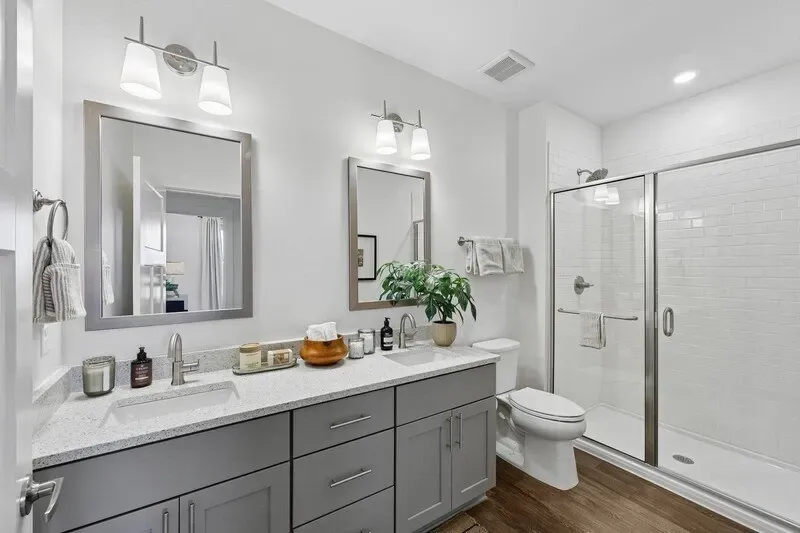 Bright modern bathroom with double vanity, mirrors, toilet, and glass walk-in shower.