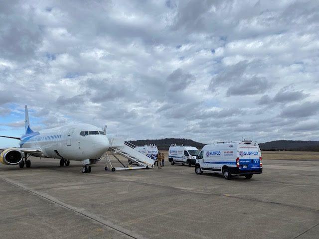 A plane is parked on the runway next to a van that says garmin on it.