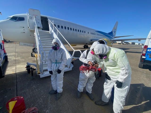 Three people in protective suits are standing in front of an airplane