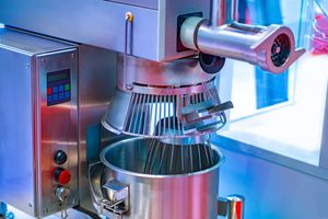 Industrial mixer blending ingredients in a stainless steel bowl in a bright kitchen