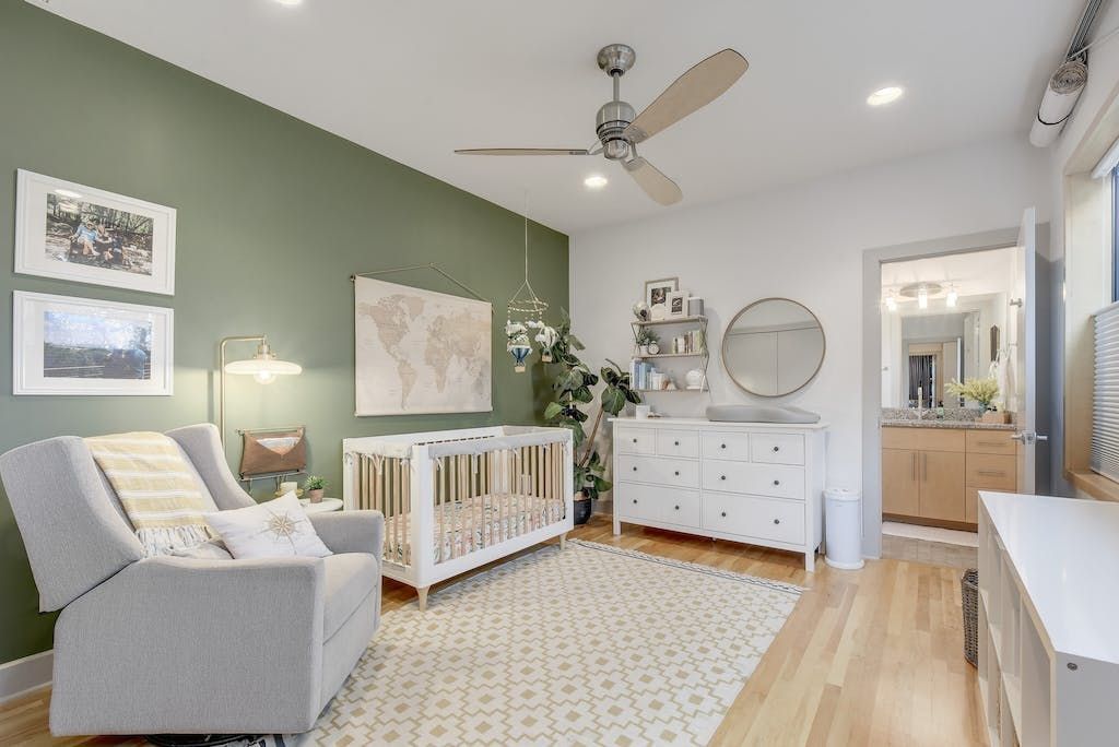 A nursery with a crib , chair , dresser and ceiling fan.