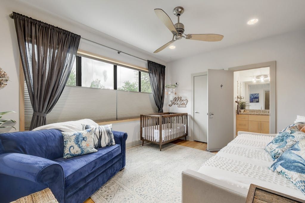 A bedroom with a couch , bed , crib and ceiling fan.