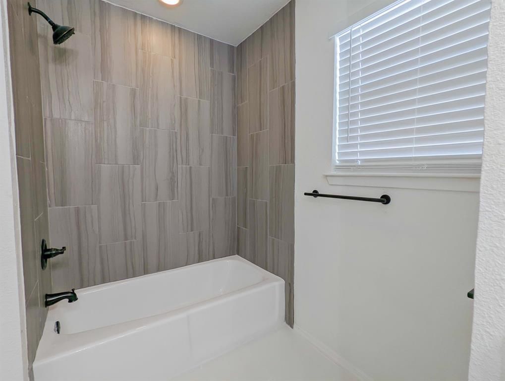A bathroom with a tub , shower , and window.