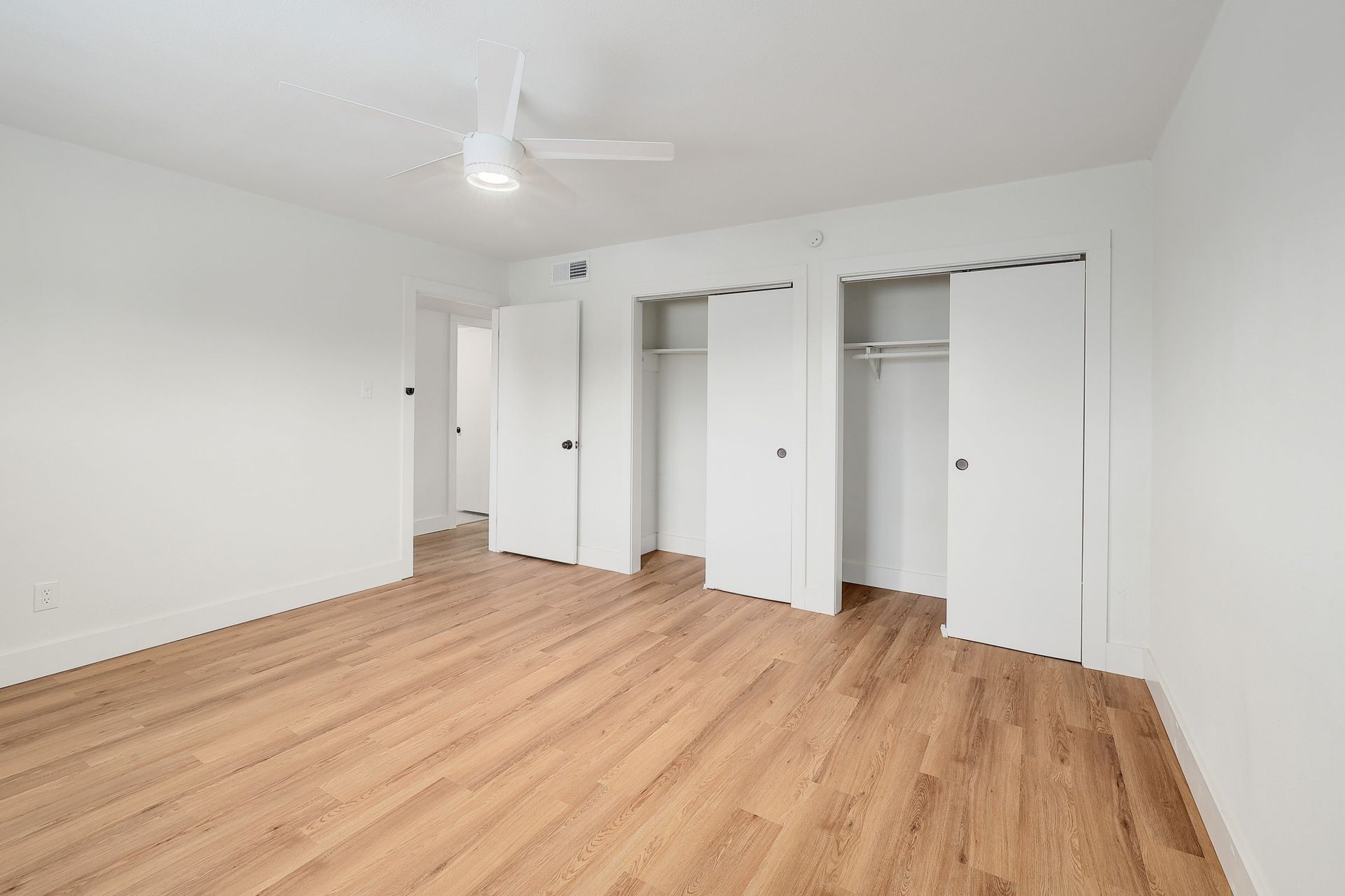 An empty bedroom with hardwood floors and a ceiling fan.