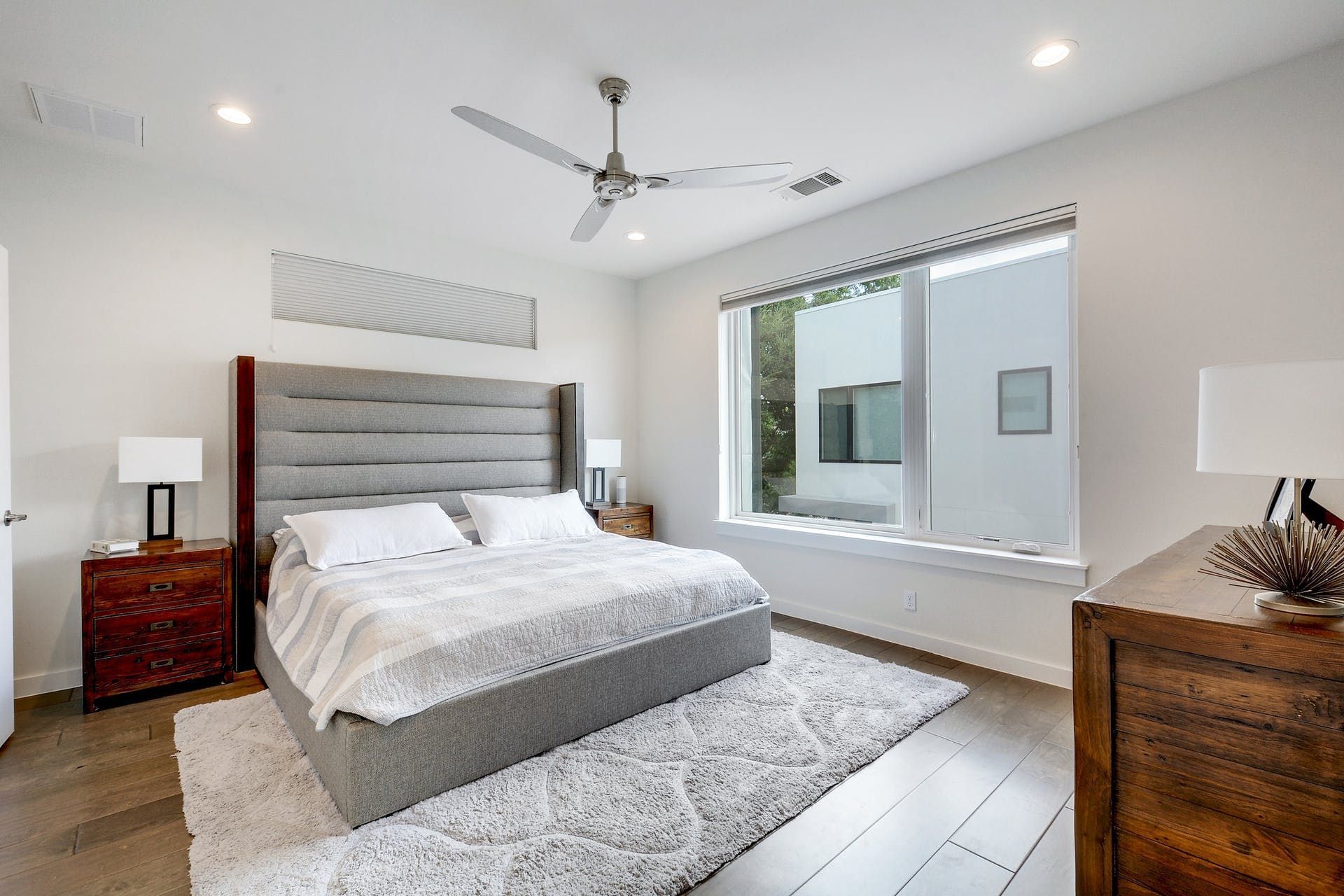 A bedroom with a bed , dresser , nightstand , rug and ceiling fan.