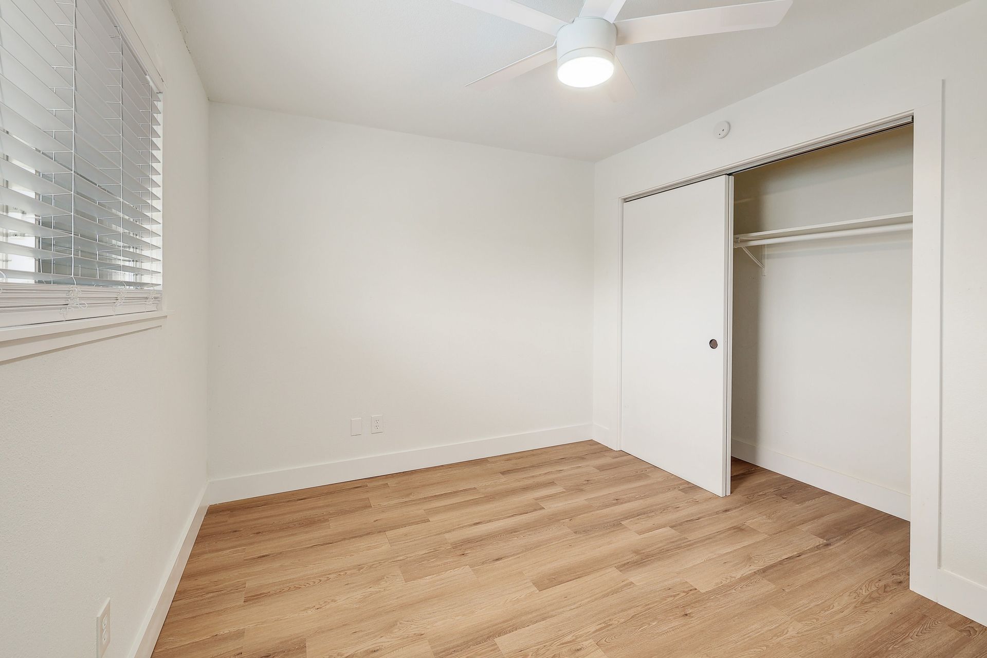 An empty bedroom with hardwood floors and a ceiling fan.