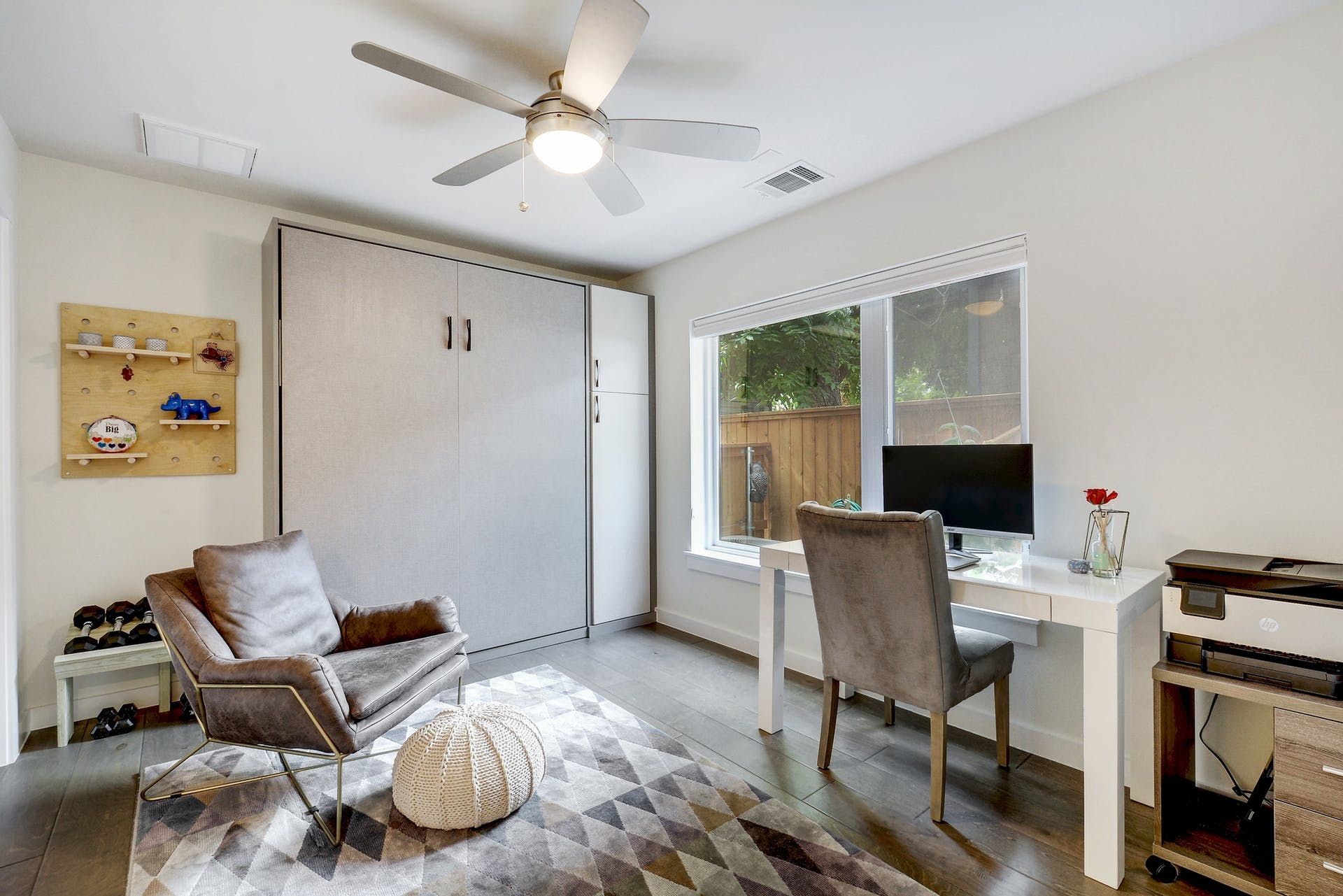 A living room with a chair , desk , computer and ceiling fan.