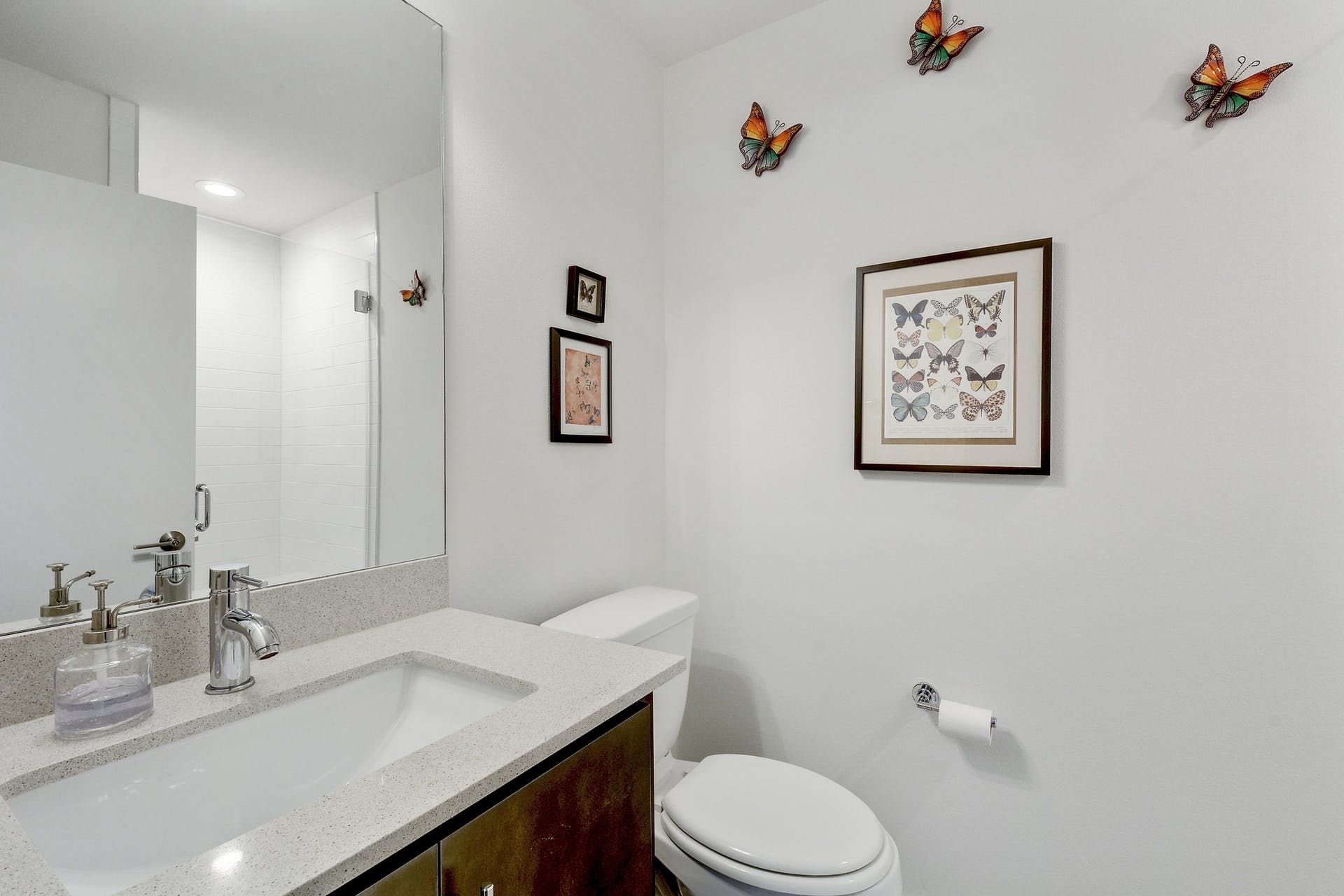 A bathroom with a sink , toilet , mirror and butterflies on the wall.